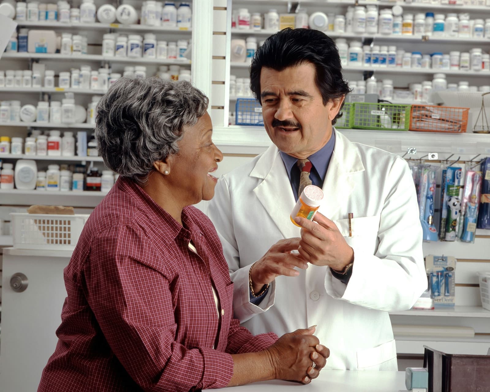 A pharmacist goes through a prescription bottle with an older patient at a pharmacy counter.